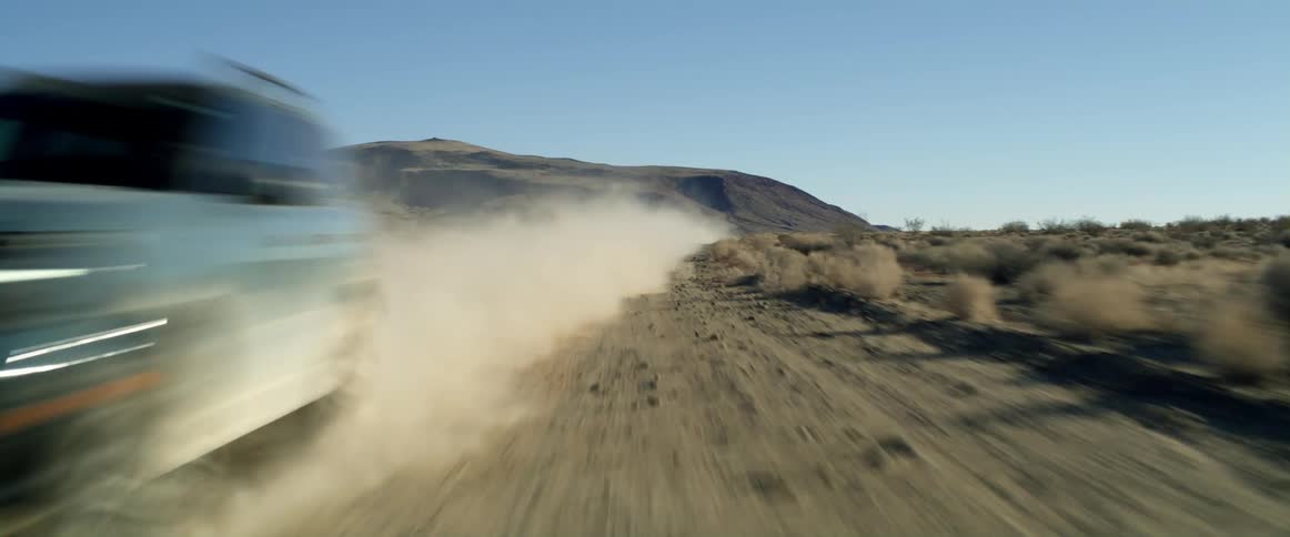 An suv speeding on a desert dirt road leaves a wake of dust