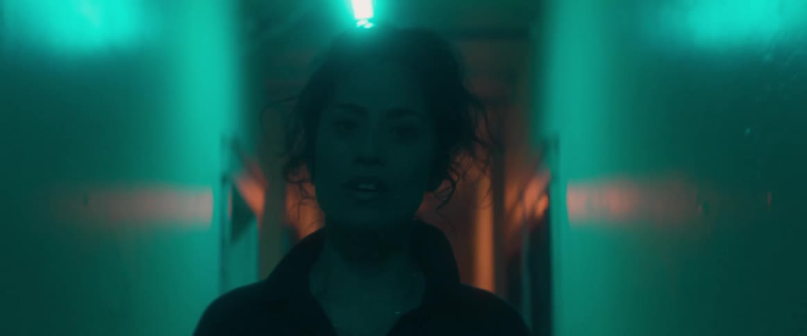 Woman moves down dark corridor lit by fluorescent lights singing