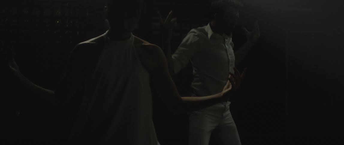 A couple dressed in all white perform a contemporary dance on a dark stage with lights flickering