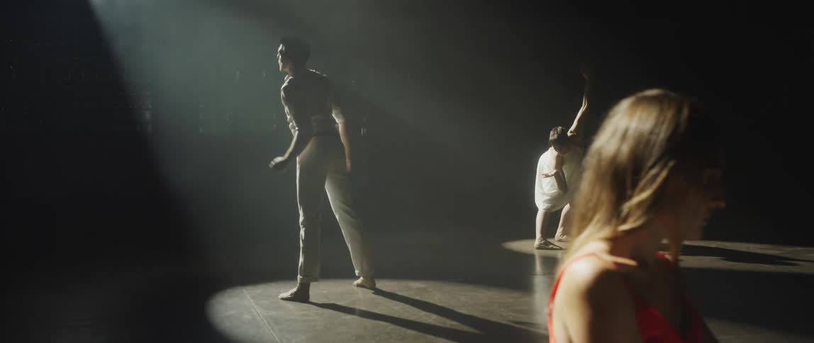A woman is playing a piano and a man and a woman are dancing behind her under spotlights