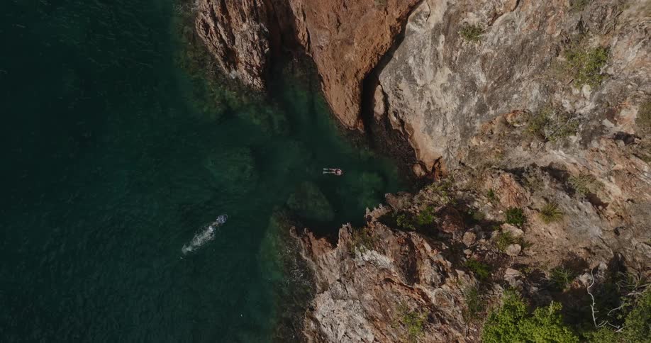 A pair of swimmers swim in the ocean near the bottom of a cliff during the day