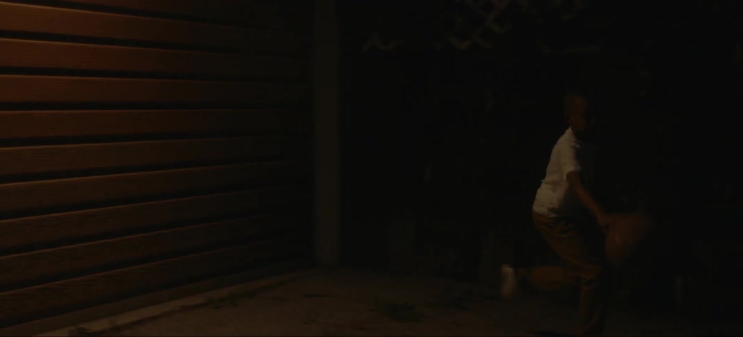 A young boy dribbles a basketball outside of a garage