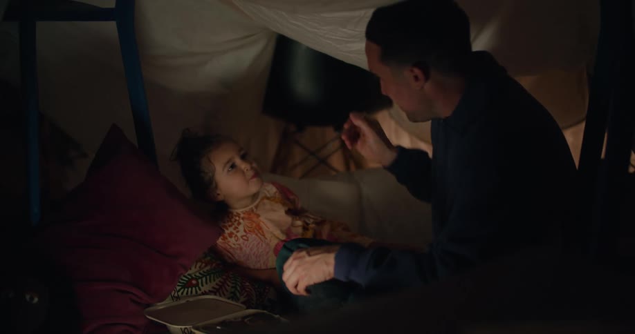 A man feeds his daughter while she sits in bed