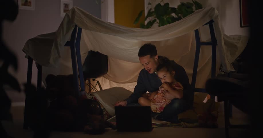 A man feeds his child while watching the laptop