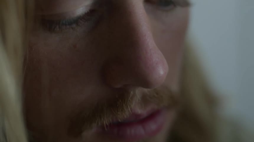 Close up view of the face of a man with long blond hair and a mustache