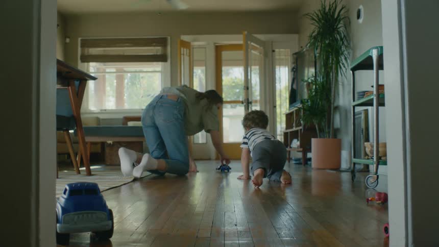 A woman and her son play with toy dinosaurs on the floor of their living room