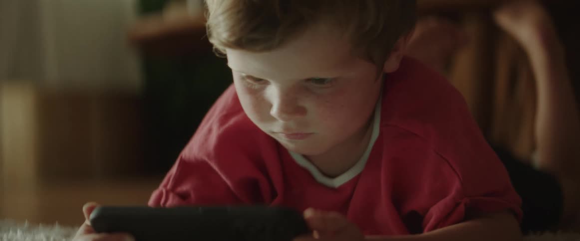 A boy is sitting in the kitchen using a device