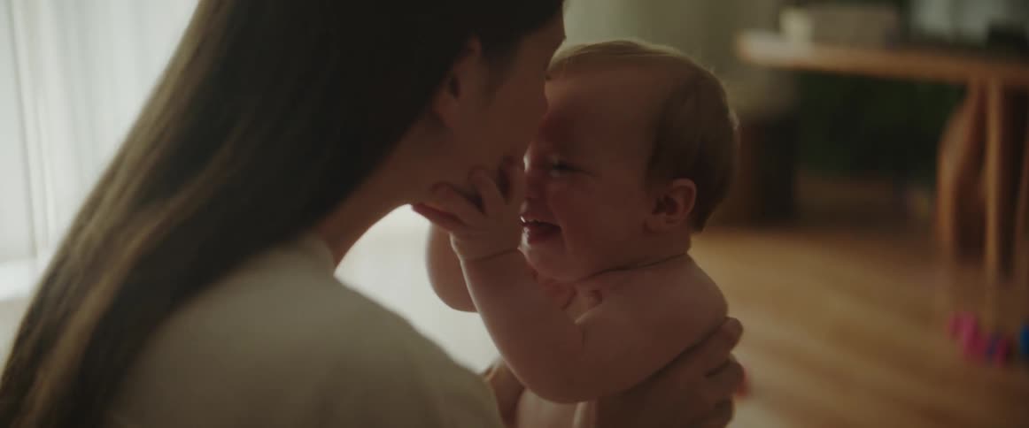 A woman is holding and kissing her baby as they smile and laugh together