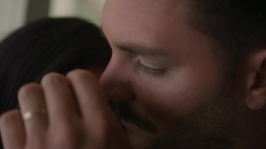 A man and woman hug and put their noses together as the man strokes the womans hair