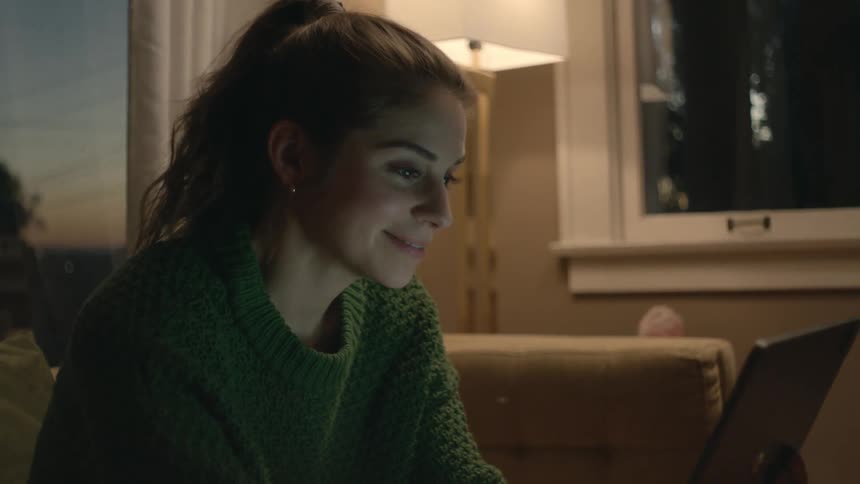 A young woman at home waves at her tablet as she video chats