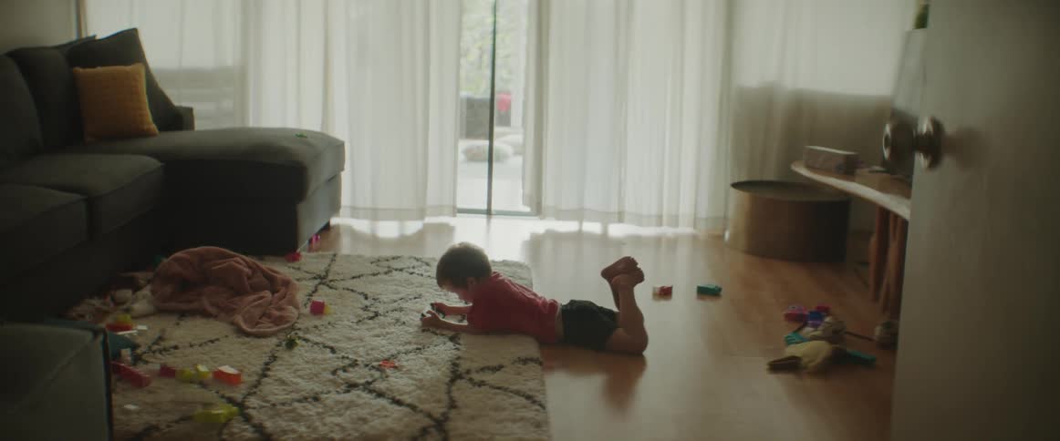 A little boy kicks his legs as he lies on his stomach watching a video on a phone