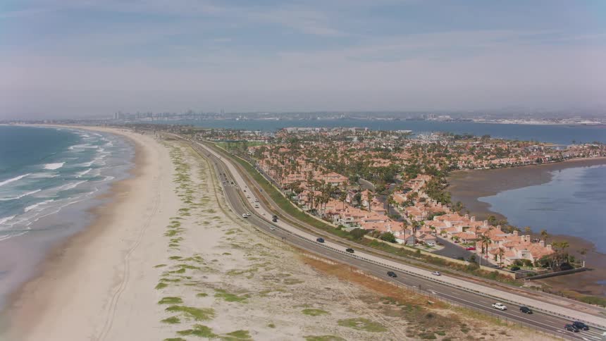 An aerial view of cars driving on the coast next to a neighborhood with a city skyline in the distance
