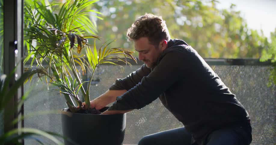 A man is sitting outside adding soil to a plant in a pot