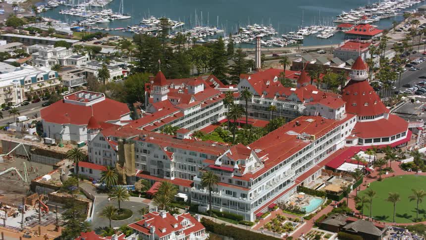 Aerial view of hotel del coronado and cars in the parking lot as waves roll over the beach along the coast