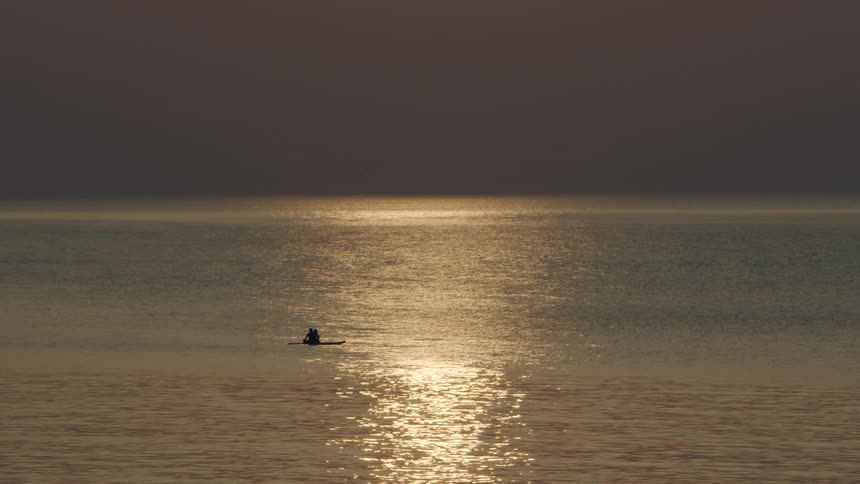 Silhouettes of two people sitting in a canoe as light from the sunset is reflecting on the water