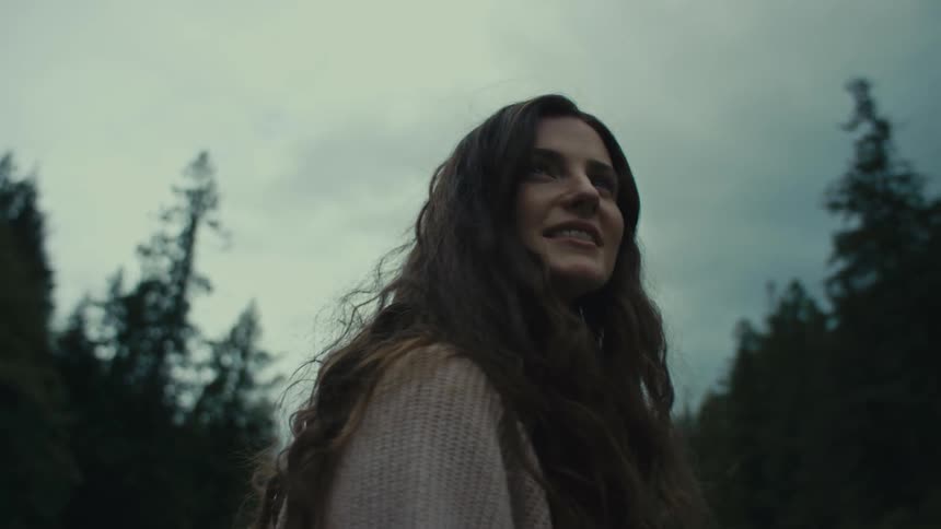 Young happy woman looks around a pine tree forest on an overcast day