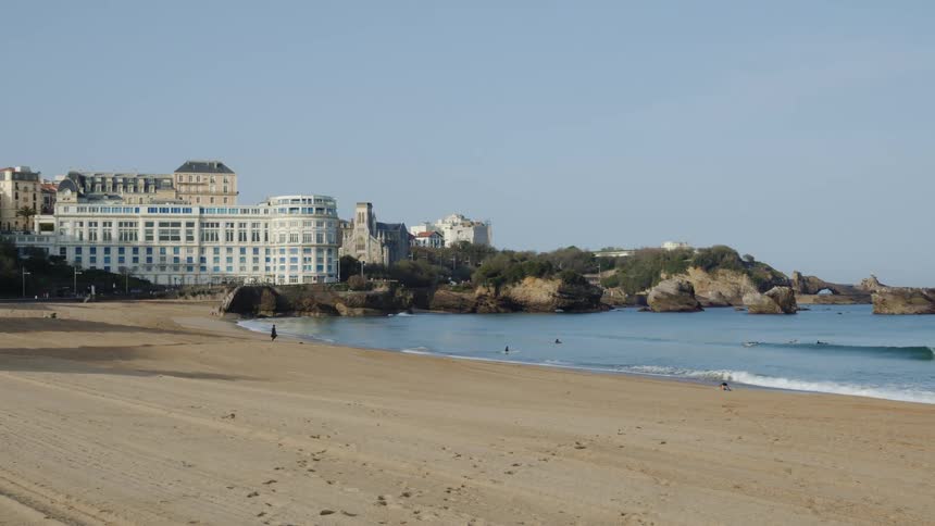 People walking on the beach and surfing in the ocean near the hotel le bellevue in biarritz france