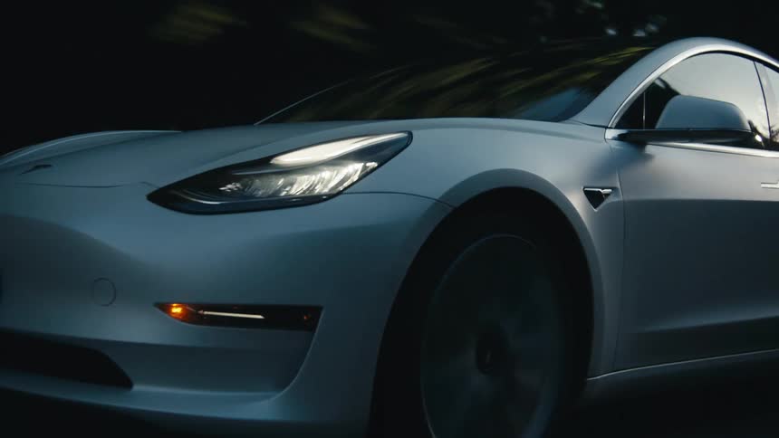 A white automobile is traveling on a forest road with the headlights on