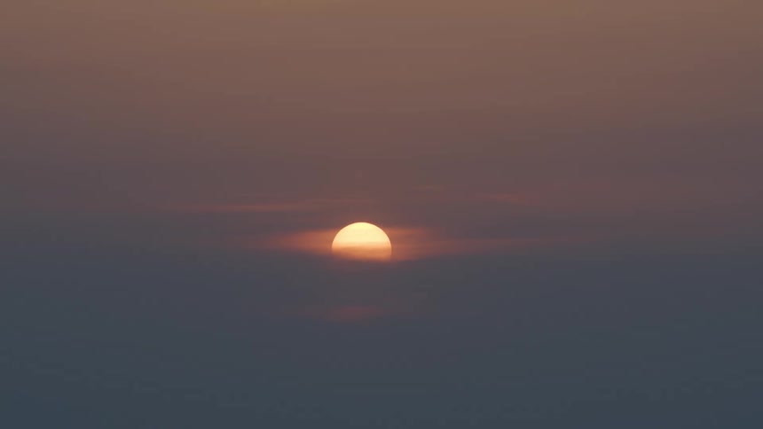 The sun sets over the ocean in a hazy red sky