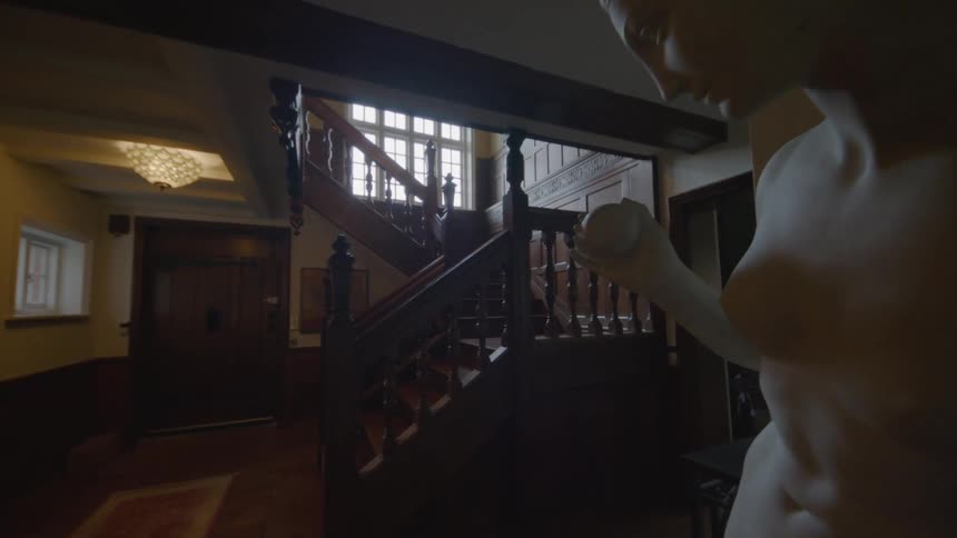 Marble statue in front a wooden staircase inside a dimly lit home at morning
