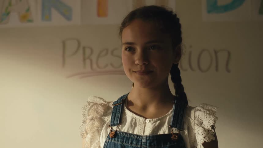 Young girl with pigtails standing in front of a whiteboard on a classroom smiles