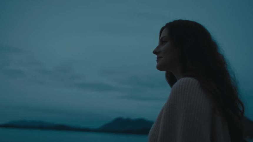 A woman is standing by the coast at sunset