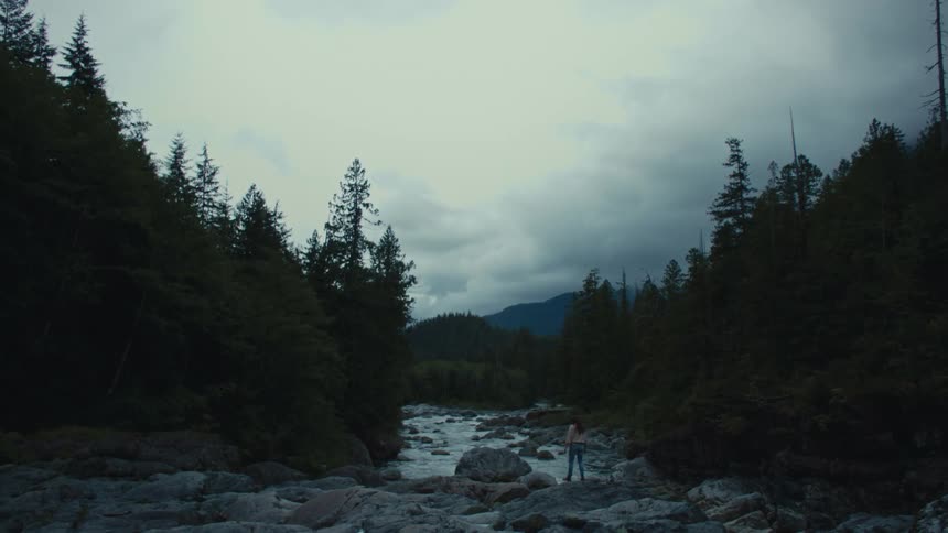 Young woman standing over the rocks near a river in the forest