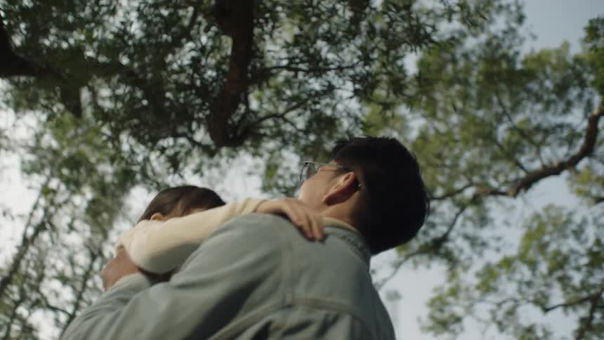 A man playfully lifts a young girl into the air outdoors during the day