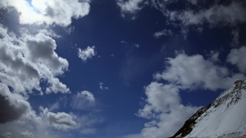 White clouds move across a blue sky above a mountain