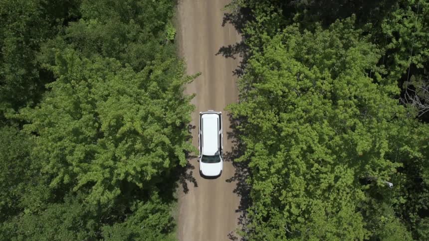 Aerial view of a car driving down a dirt road surrounded by trees