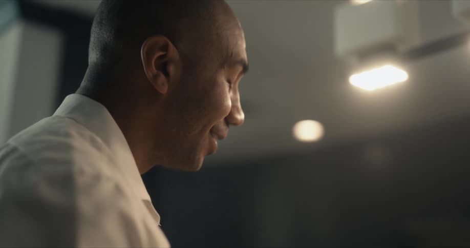 Man looks up nodding and smiling as he converses with another man while working