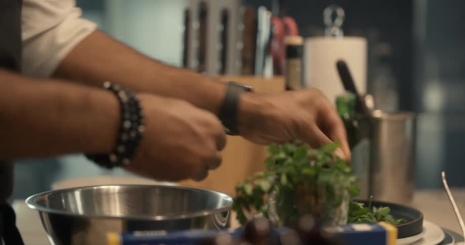 Cook standing in kitchen plucks fresh herbs and adds to bowl