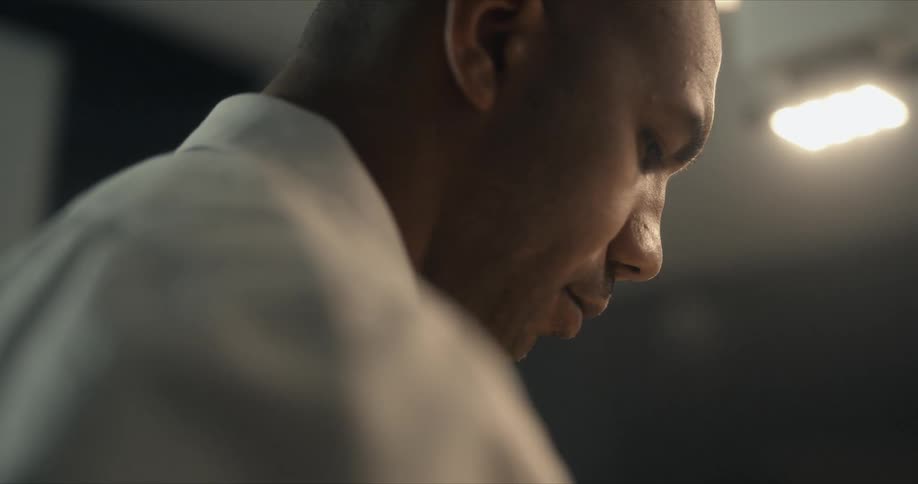 A man is in a lit room looking down as he makes small movements