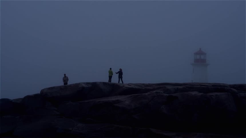Three people stand on a rock platform near a lighthouse