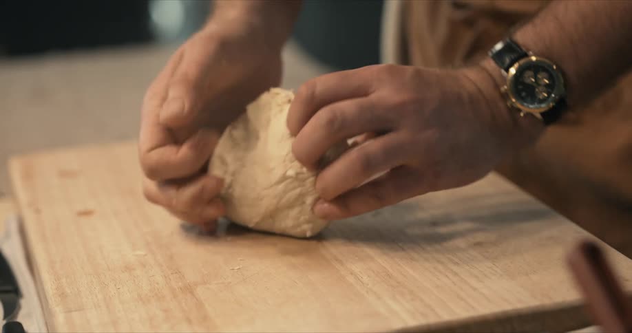 A man kneads dough on a wooden cutting board in a kitchen