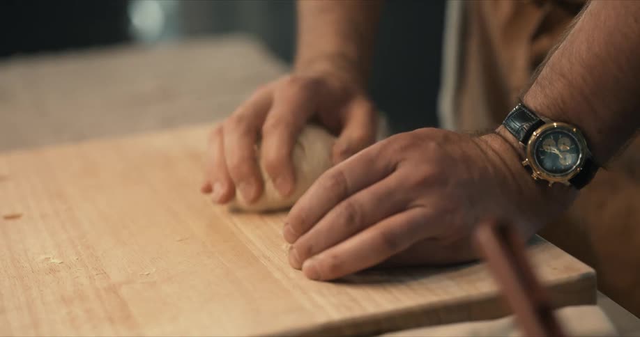 A man kneads dough on a wooden cutting board