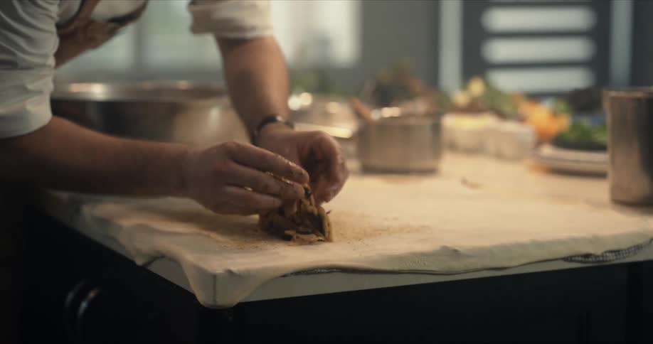 A chef uses his hands to scoop food from a bowl and place it onto dough spread out on the table