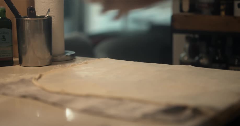 A male chef is sprinkling flour onto flattened dough on a counter top