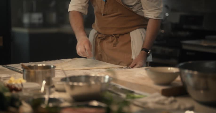 A chef carefully stretches dough out on a floured counter
