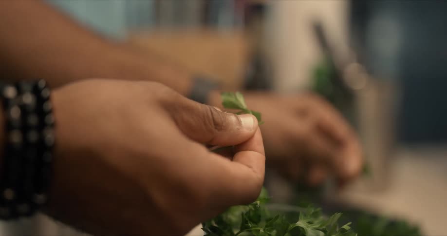 A man picks the parsley leaves off the stems in the kitchen