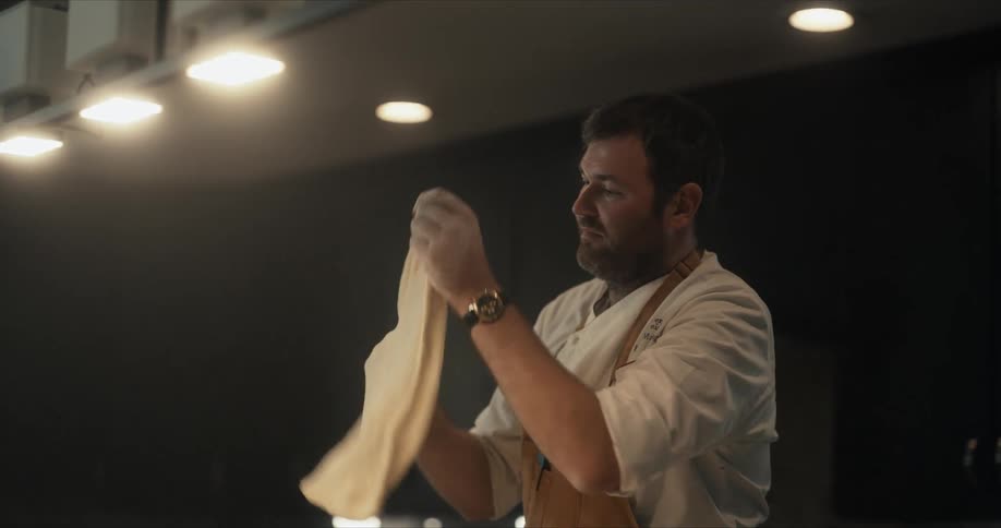 A man is stretching pizza dough with his hands in a kitchen
