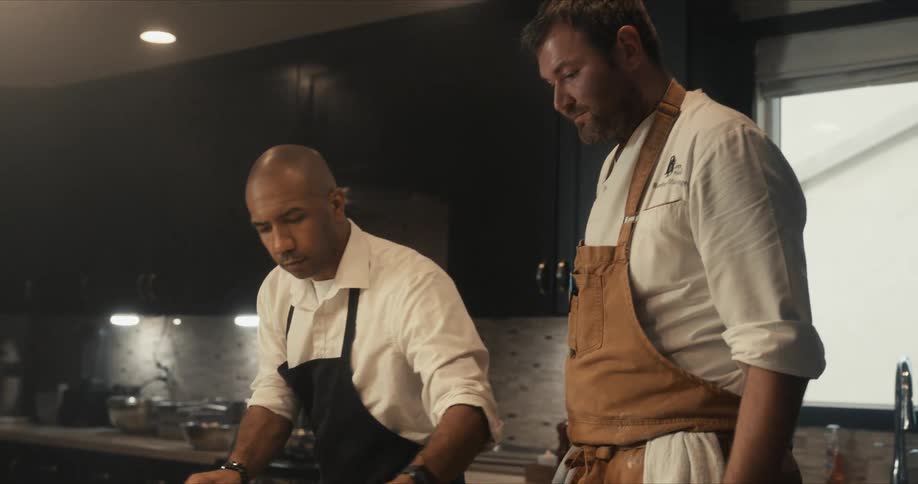 A chef uses a brush to glaze food before another chef carries the food away to place it in the oven