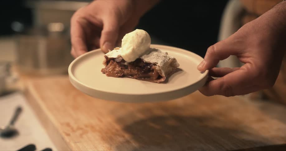 A cook lifts a plate of food from a cutting board and presents it to the camera