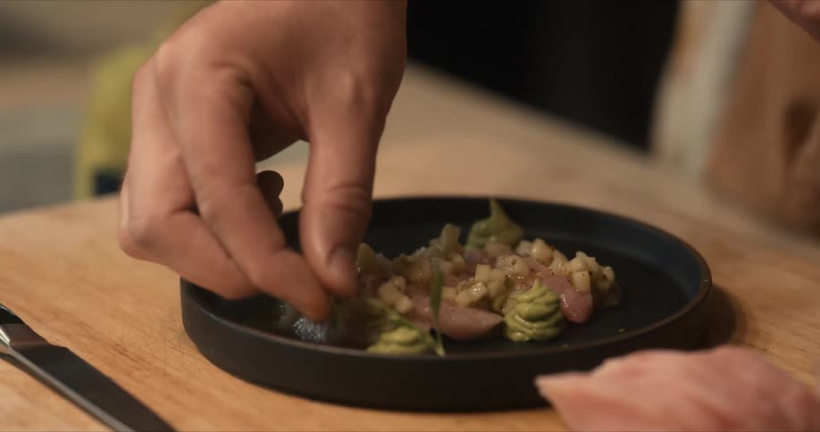 A chef places herbs on a plate of food