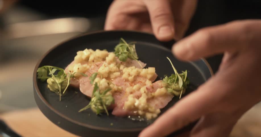 Chef presents a dish served on a small black circular plate