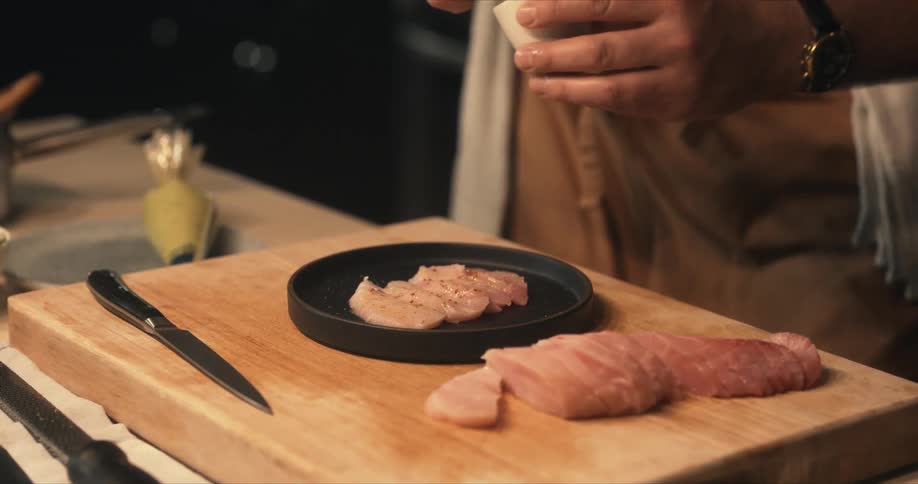 A chef sprinkles seasoning on sliced pieces of fish