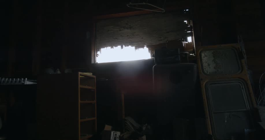 A window partially covered with a tattered blind in a storage area full of junk