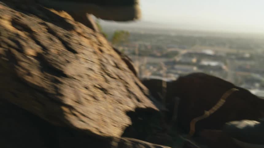The sun shines brightly on the feet of someone walking up a rocky hill overlooking a valley
