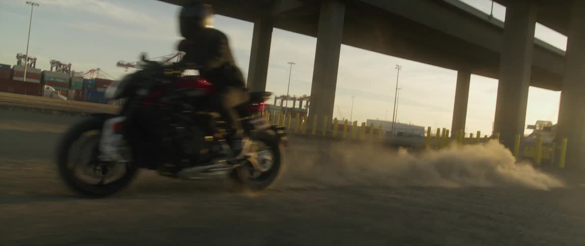 A person rides a motorcycle through the dirt under a bridge during the day