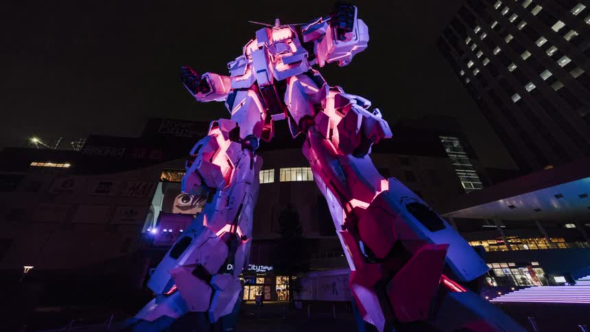 Lights are flashing on a giant robot standing outside near tall buildings at night